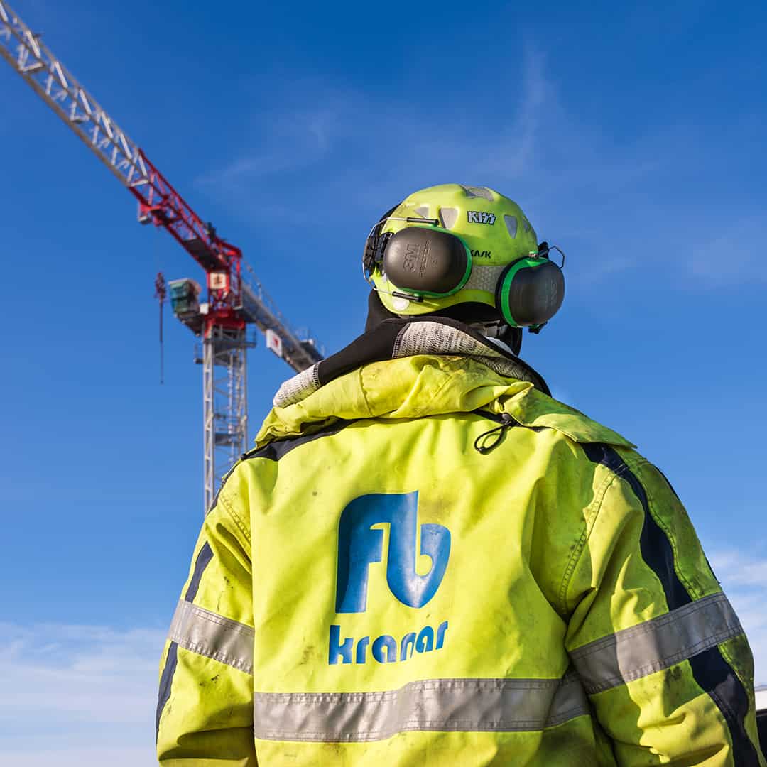 Kranoperatör i skyddskläder med en tornkran i bakgrunden under en klar himmel.