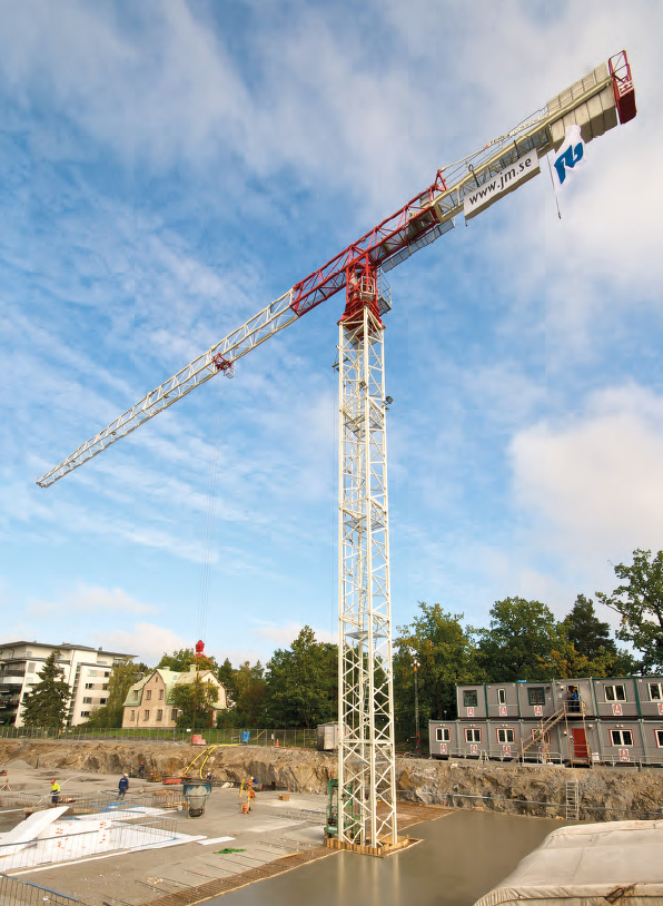 Tower crane operating at a construction site with workers laying foundations.